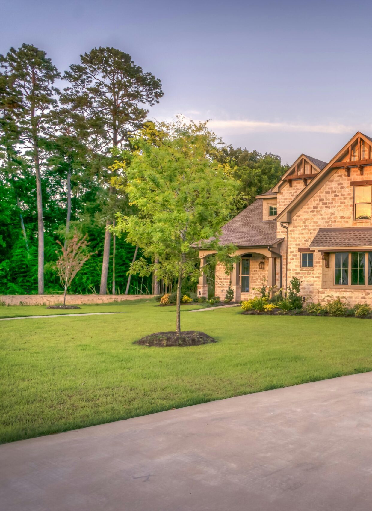 Elegant stone family home surrounded by trees, lush lawn, and vibrant garden.